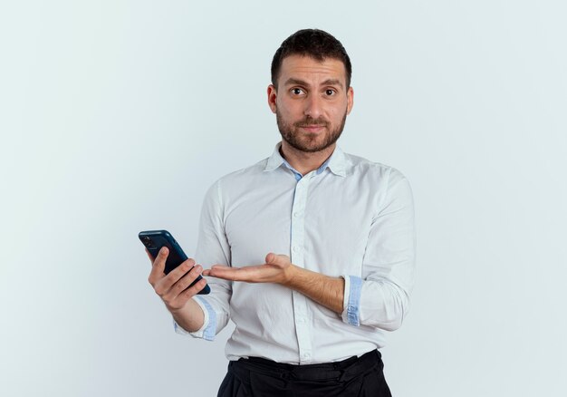 Tevreden knappe man houdt en wijst naar telefoon geïsoleerd op een witte muur