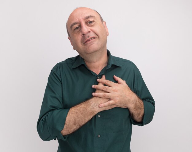 Tevreden man van middelbare leeftijd met een groene t-shirt hand op hart zetten geïsoleerd op een witte muur