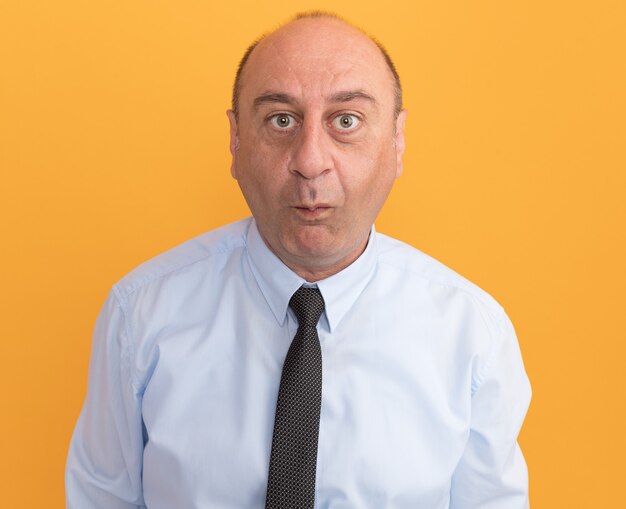 Tevreden man van middelbare leeftijd met een wit t-shirt met stropdas die kusgebaar toont dat op oranje muur wordt geïsoleerd