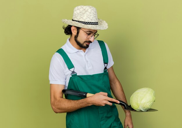 Tevreden mannelijke tuinman in optische bril met tuinhoed houdt kool op schop