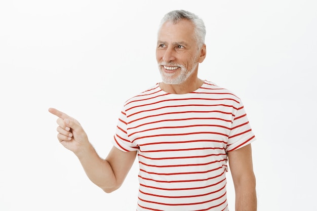 Tevreden oude man in t-shirt die naar links kijkt en wijst