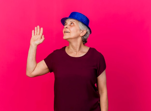 Tevreden oudere vrouw met feestmuts staat met opgeheven hand opzoeken op roze