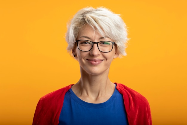 Tevreden supervrouw met rode cape in optische glazen kijkt voorzijde geïsoleerd op oranje muur