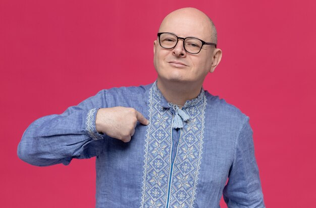 Tevreden volwassen man in blauw shirt met een bril die naar zichzelf wijst