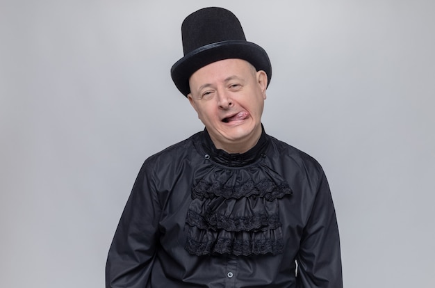 Tevreden volwassen Slavische man met hoge hoed en in zwart gothic shirt steekt tong uit