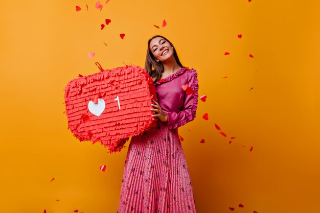 Tevreden vrouw in roze outfit lachen. Aanbiddelijk Kaukasisch meisje in lange rok die zich op gele muur bevindt.