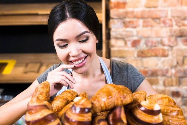 Tevreden vrouwelijke bakker die vers gebakken croissant bekijkt