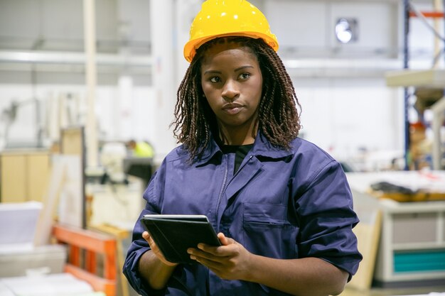 Tevreden vrouwelijke fabrieksarbeider die zich met tablet bevindt en wegkijkt