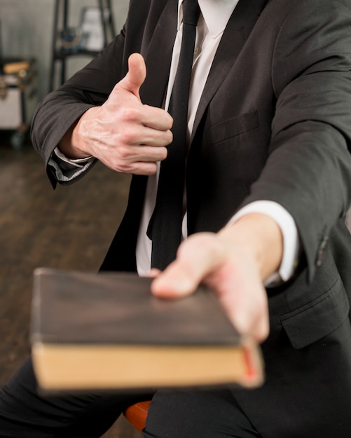 Tevreden zakenman die boek geeft dat duim toont