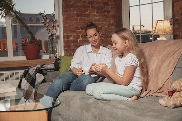 Thee drinken, praten. Moeder en dochter tijdens zelfisolatie thuis in quarantaine, gezellige familietijd, comfort, huiselijk leven. Vrolijke, blij lachende modellen. Veiligheid, preventie, liefdesconcept.