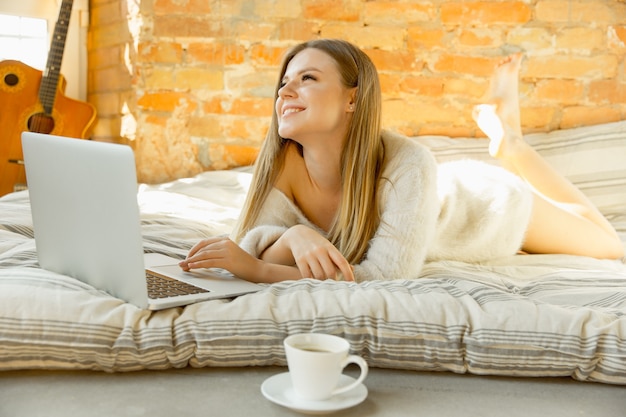 Thuis relaxen. Mooie jonge vrouw die op matras met warm zonlicht ligt. Blond vrouwelijk model heeft weekendtijd om uit te rusten