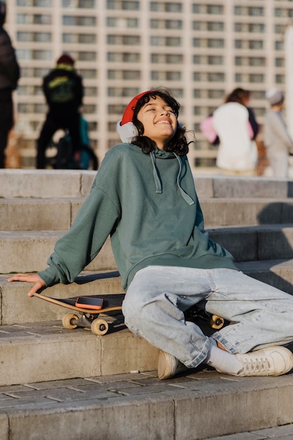 Tiener buiten genieten van muziek op koptelefoon zittend op skateboard