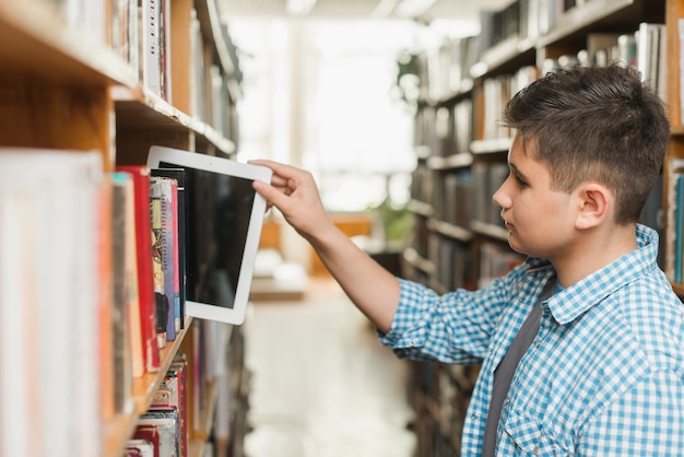 Gratis foto tiener die tablet op boekenrek zet