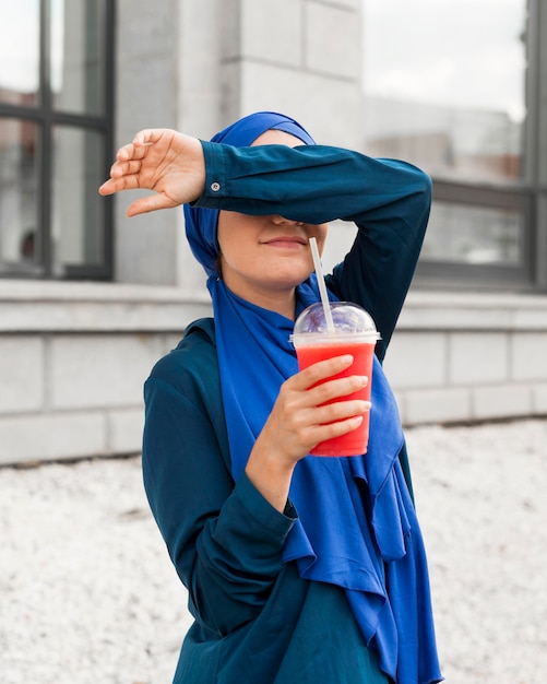 Gratis foto tiener houdt een smoothie terwijl ze haar ogen bedekt met haar arm
