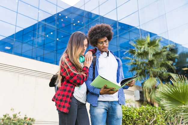 Tiener mannelijke en vrouwelijke studenten die het boek lezen dat zich tegen het universitaire gebouw bevindt