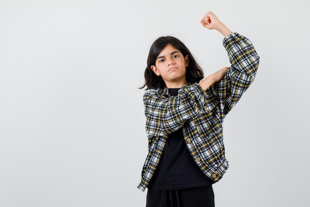 Tiener meisje hand op armspieren in casual shirt en peinzend op zoek. vooraanzicht.