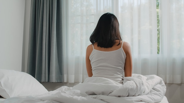 Tiener Spaanse vrouw wordt thuis wakker. Het jonge Aziatische meisje uitrekken zich de hele nacht na wakkere slaap beginnend met een nieuwe dag met energie en vitaliteit voelde zeer verfrist op bed dichtbij venster in slaapkamer bij ochtend.