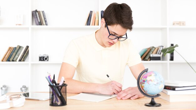 Tiener student in glazen aan tafel zitten en schrijven