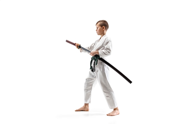 Tienerjongen die bij Aikido-opleiding in martial arts-school vecht. Gezonde levensstijl en sportconcept. Fightrer in witte kimono op witte muur. Karateman met geconcentreerd gezicht in uniform.