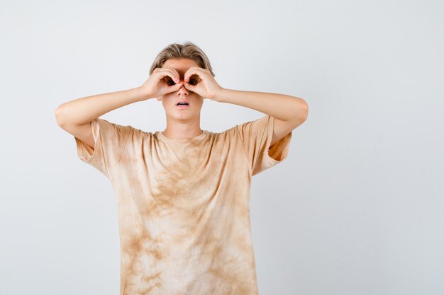 Tienerjongen in t-shirt die een glazen gebaar toont en zich afvraagt, vooraanzicht.