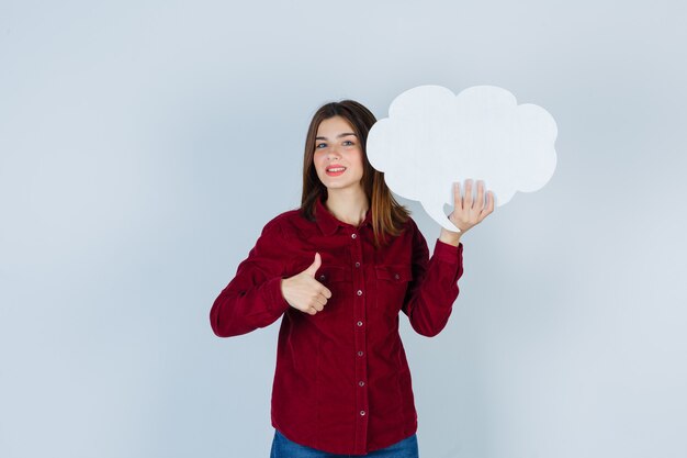 Tienermeisje in bordeauxrood shirt met tekstballon, duim opdagen en vrolijk kijken, vooraanzicht.