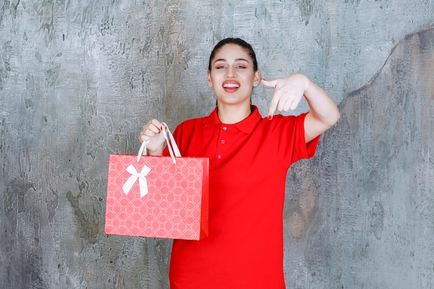 Tienermeisje in rood shirt met een rode boodschappentas en glimlachend met verrassing.