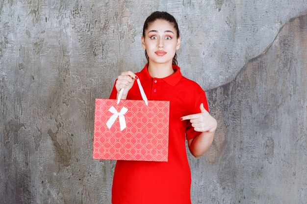 Tienermeisje in rood shirt met een rode boodschappentas en ziet er bang en doodsbang uit.