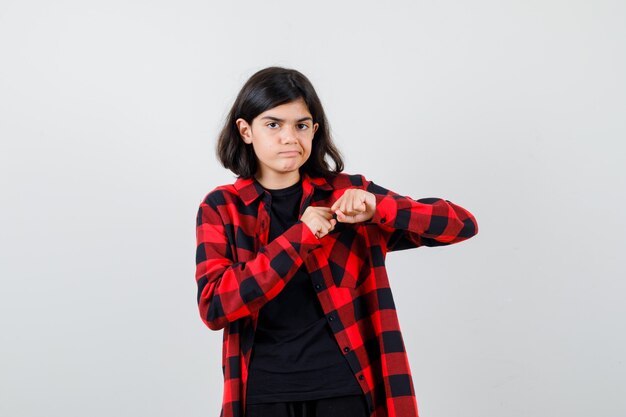 Tienermeisje staat in gevecht pose in t-shirt, geruit hemd en ziet er roekeloos uit. vooraanzicht.