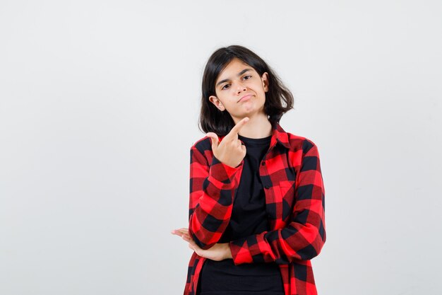 Tienermeisje wijst naar de rechterbovenhoek in t-shirt, geruit hemd en ziet er zelfverzekerd uit. vooraanzicht.