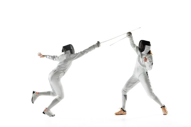 Tienermeisjes in het schermen van kostuums met zwaarden in handen die op witte studiomuur worden geïsoleerd