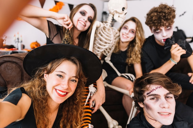 Tieners in grimmige en alloween kostuums en skelet doen selfie en glimlachen