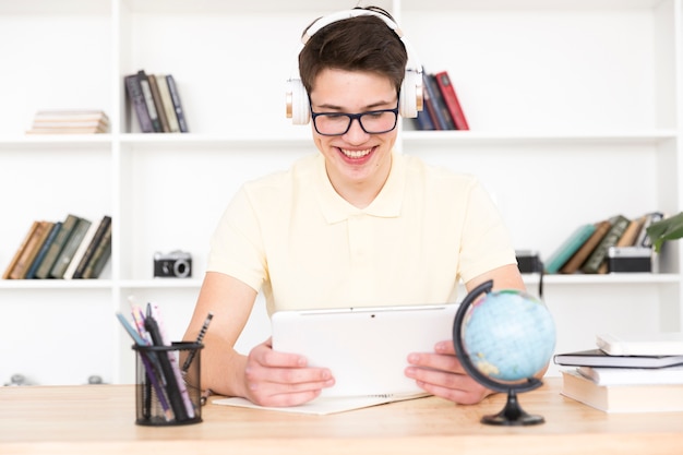 Tienerstudent in glazen die bij lijst zitten en pret met tablet hebben