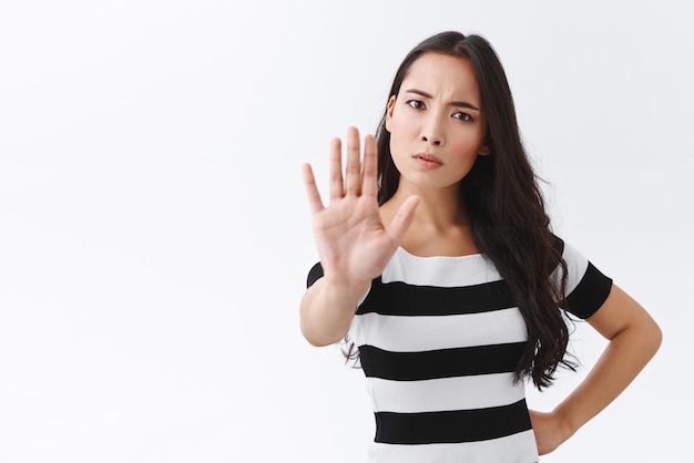 Tijd om te vertragen en te stoppen Serieus uitziende boze jonge zelfverzekerde vrouw hand naar voren trekken en staren camera verontrust iets verbieden maken verbod gebaar staan witte achtergrond