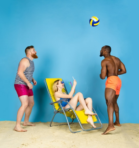 Tijd voor activiteit. Gelukkige vrienden nemen selfie, volleyballen op blauwe studio achtergrond. Concept van menselijke emoties, gezichtsuitdrukking, zomervakantie of weekend. Chill, zomer, zee, oceaan.