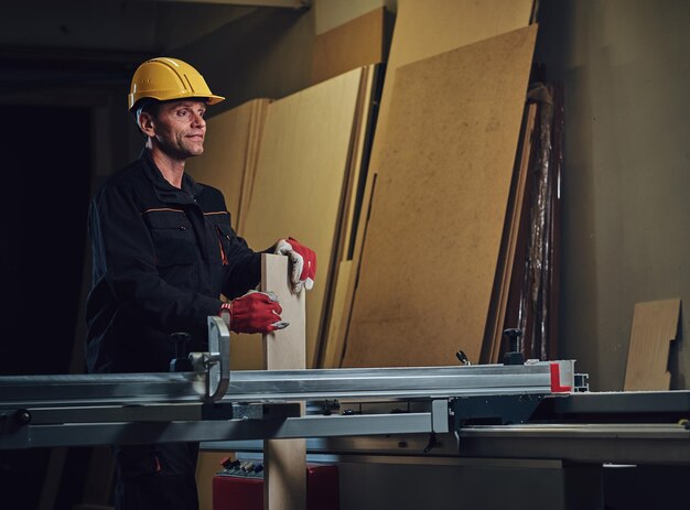 Timmerman man gekleed in een gele veiligheidsdop werkt met kettingzaag in een garage.