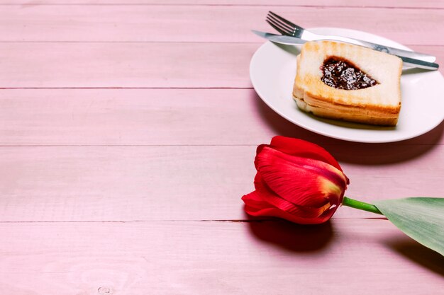 Toast met jam in hartvorm met rode tulp