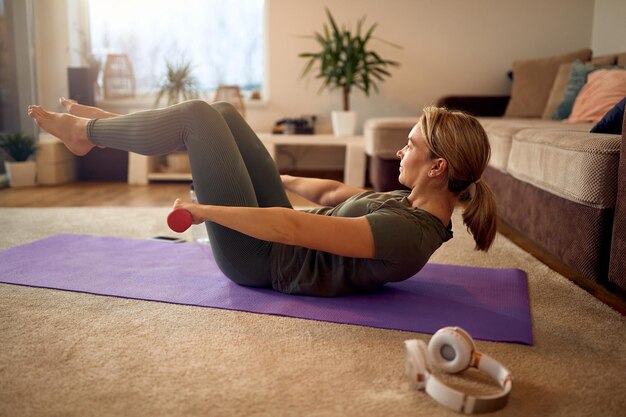 Toegewijde sportvrouw die dumbbells gebruikt tijdens het oefenen van situps tijdens thuistraining