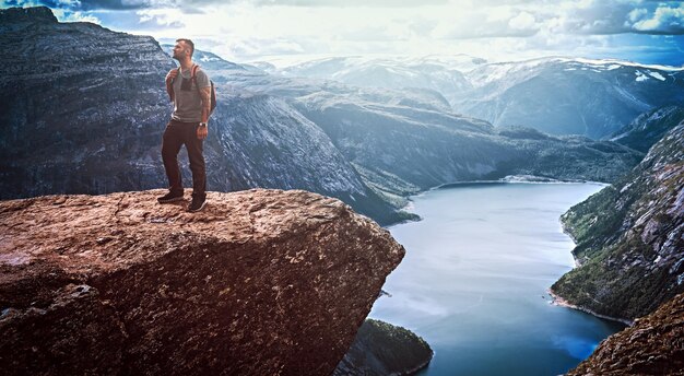 Toeristische man die in de Trolltunga staat en geniet van het prachtige uitzicht op de Noorse fjord.