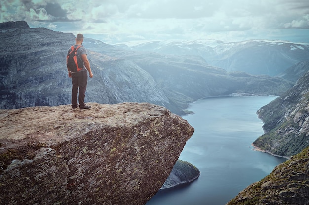 Toeristische man die in de trolltunga staat en geniet van het prachtige uitzicht op de noorse fjord.
