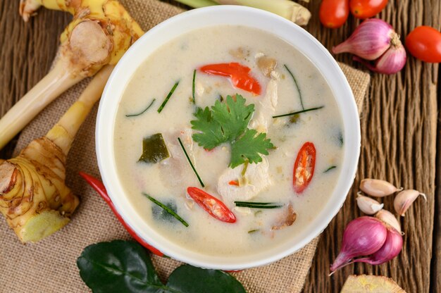 Tom Kha Kai in een kom met kaffir limoenblaadjes, citroengras, rode ui, laos en chilipeper.