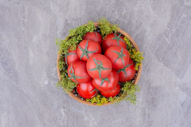 Tomaten in een houten beker met kruiden rond.