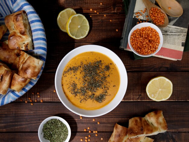 Tomaten linzensoep met kruiden in een witte kom geserveerd met brood, bovenaanzicht