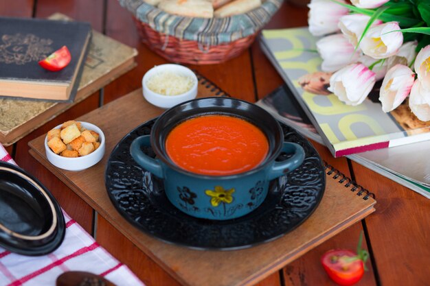 Tomatensoep in een pot met gehakte parmezaanse kaas en broodcrackers.