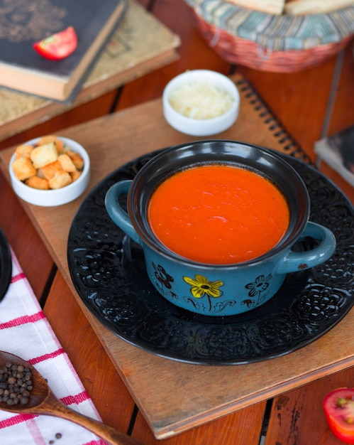 Tomatensoep in een pot met gehakte parmezaanse kaas en broodcrackers.