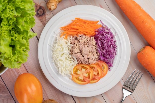 Tonijnsalade met wortelen, tomaten, kool op een witte plaat op een houten vloer.