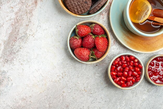 Top close-up weergave aardbeien een kopje zwarte thee met citroen kommen aardbeien koekjes zaden van granaatappel op tafel