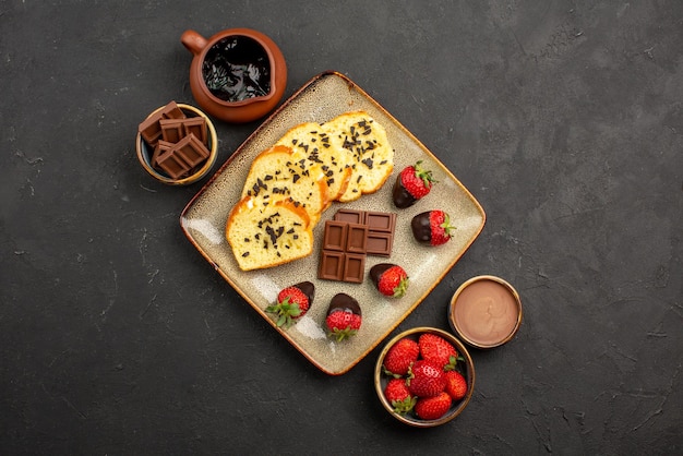 Top close-up weergave chocolade aardbeien cake aardbeien chocolade crème en chocolade in kommen smakelijke cake en aardbeien in het midden van de donkere tafel