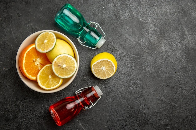 Gratis foto top close-up weergave citrusvruchten citrusvruchten in kom naast de kleurrijke flessen op de donkere tafel
