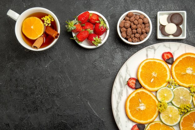 Top close-up weergave een kopje thee smakelijk gerecht van citrusvruchten en aardbeien naast de kommen van chocolade aardbeien en hazelnoten en kopje thee met citroen