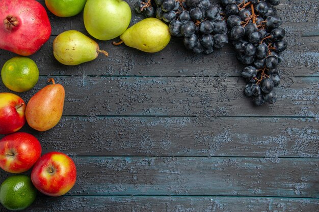 Top close-up weergave fruit granaatappel appels peren limoenen en druiven zijn neergelegd in een cirkel op donkere tafel